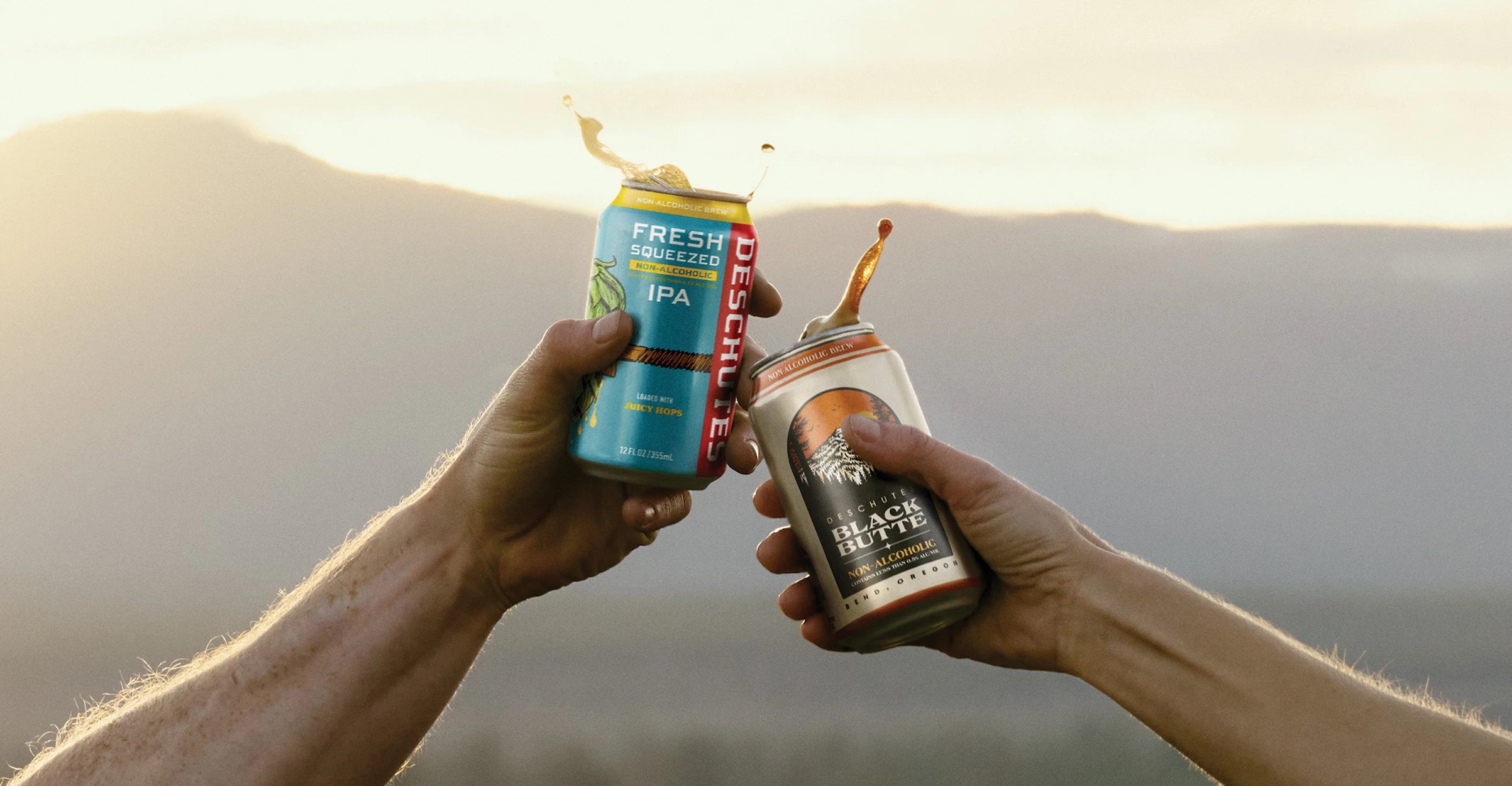 Two hands tapping cans of Fresh Squeezed Non-Alcoholic IPA and Black Butte Non-Alcoholic together.